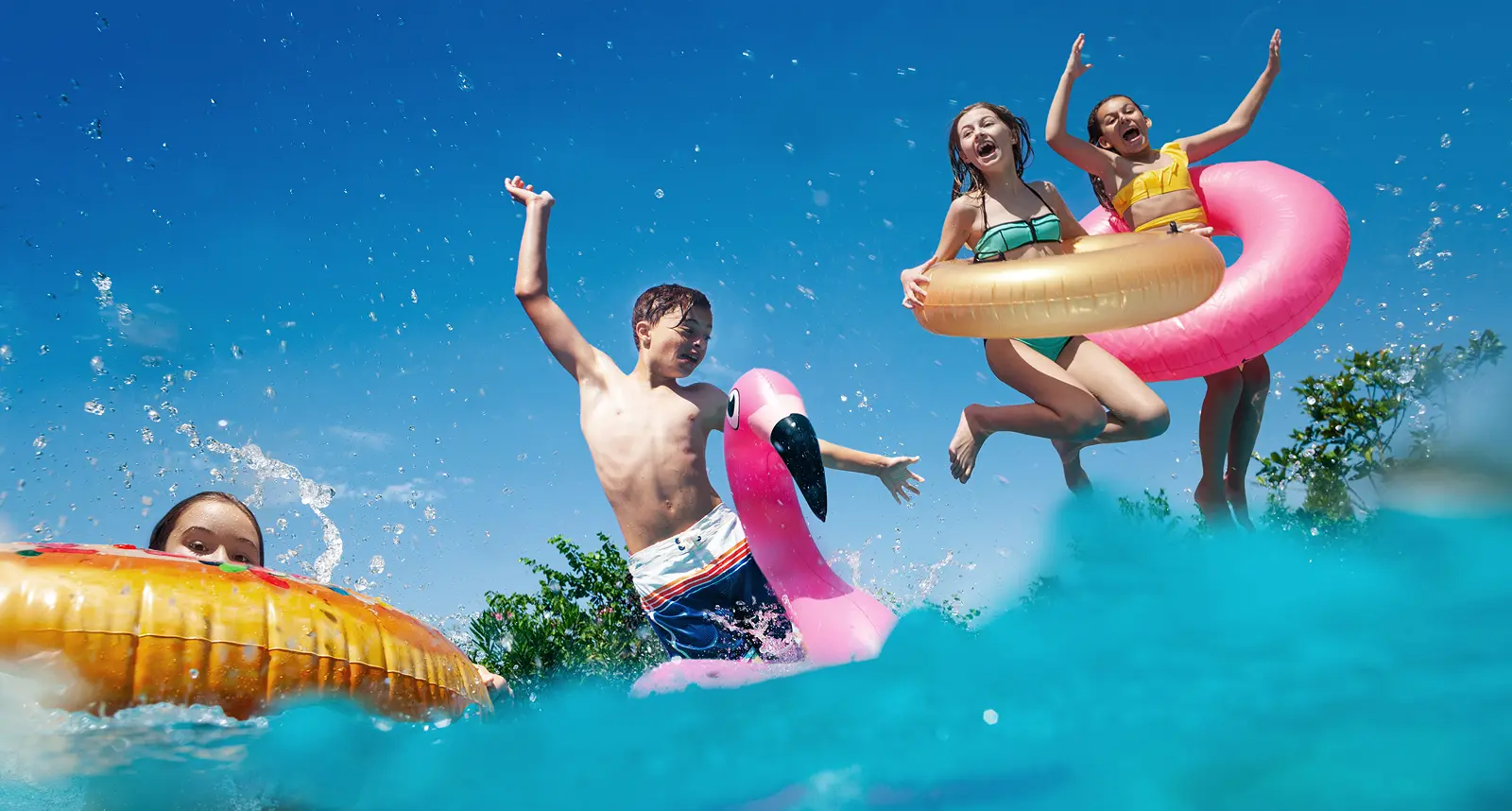 Four children with pool floats jump and play in a Grand Magnolia swimming pool on a sunny day.