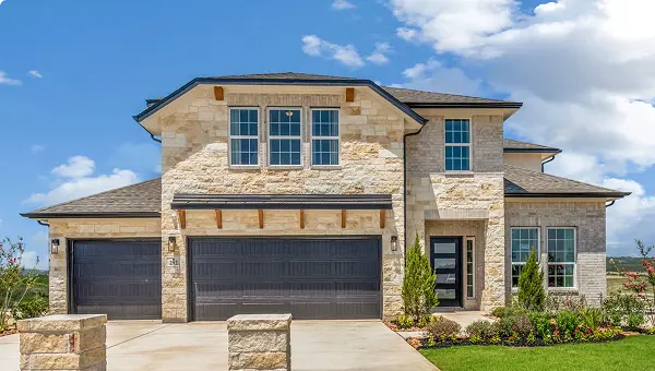 Two-story modern stone house in Grand Magnolia, Magnolia TX with three-car garage and landscaped yard.