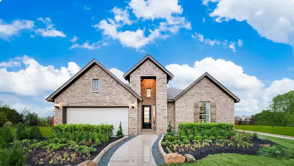 Modern brick house with two-car garage in Magnolia TX’s lagoon community, blue sky above.