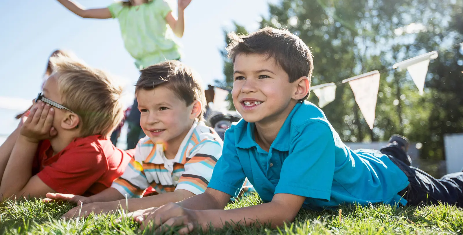 Three boys lie on grass in Grand Magnolia, with bunting and another child enjoying the sunny day.