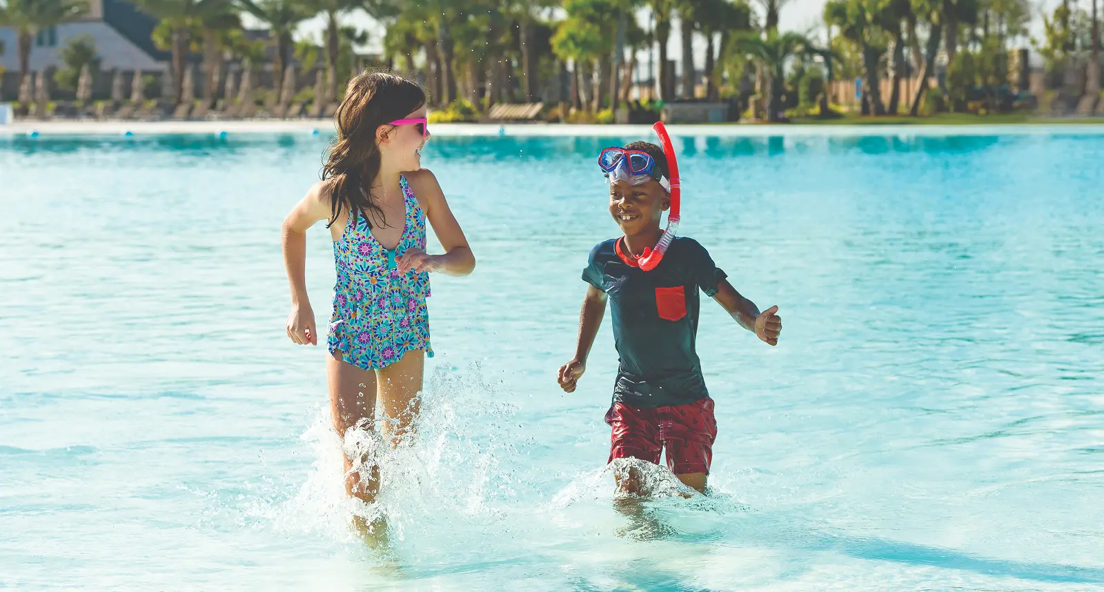 Two children in swimwear splash in shallow water at a lagoon community in Magnolia, TX.