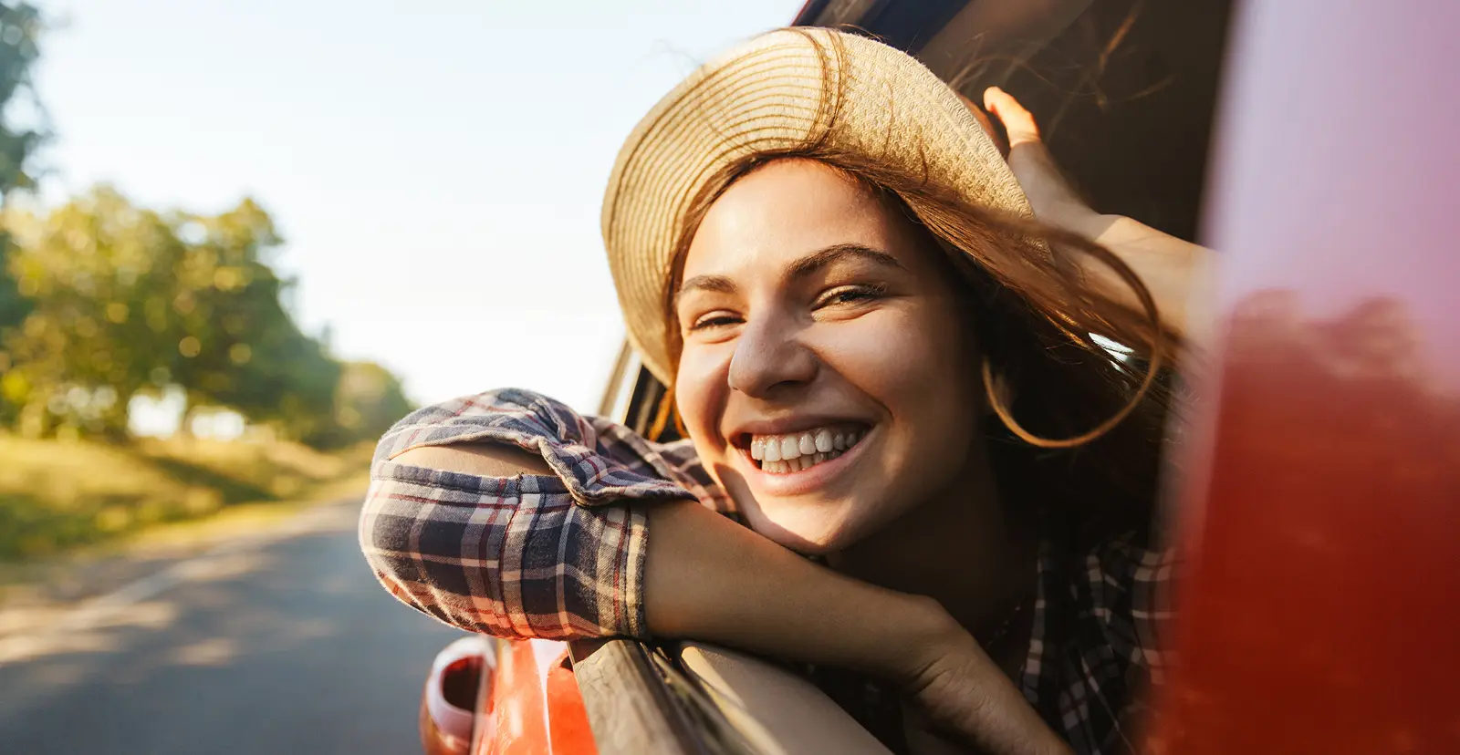 Smiling person in a plaid shirt leans out of a car window in Grand Magnolia on a sunny day.